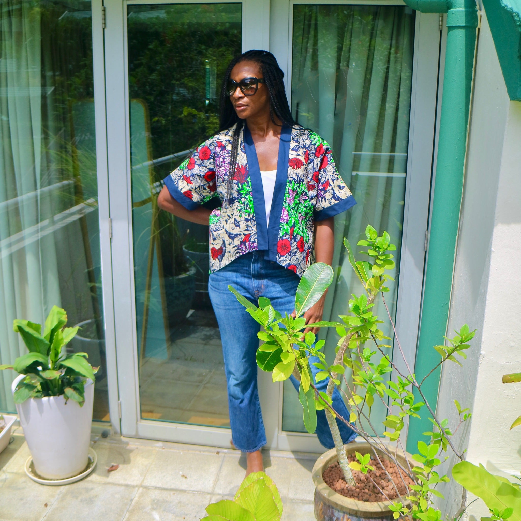 Woman in a floral kimono standing in front of a glass door with plants around.