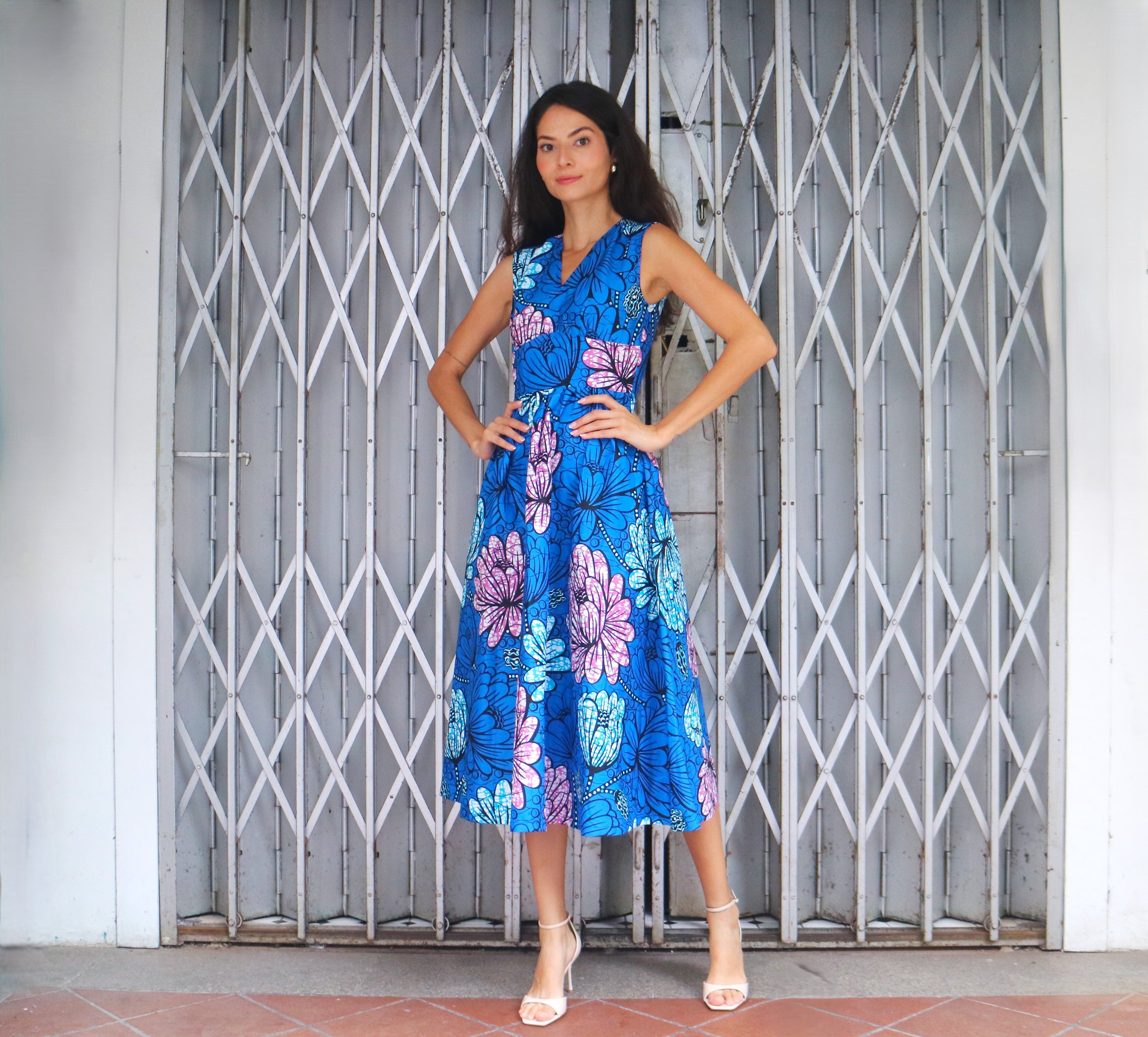Woman wearing a blue floral dress standing in front of a metal gate.