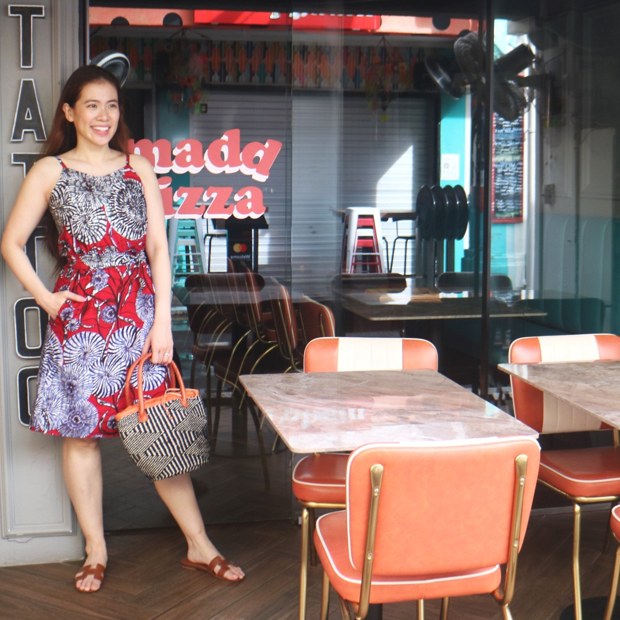 Woman standing in front of a pizza restaurant with tables and chairs inside.
