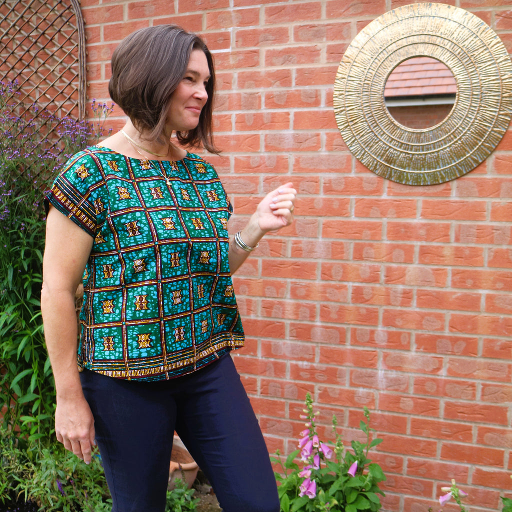 Woman wearing a patterned top standing in front of a brick wall with decorative elements.