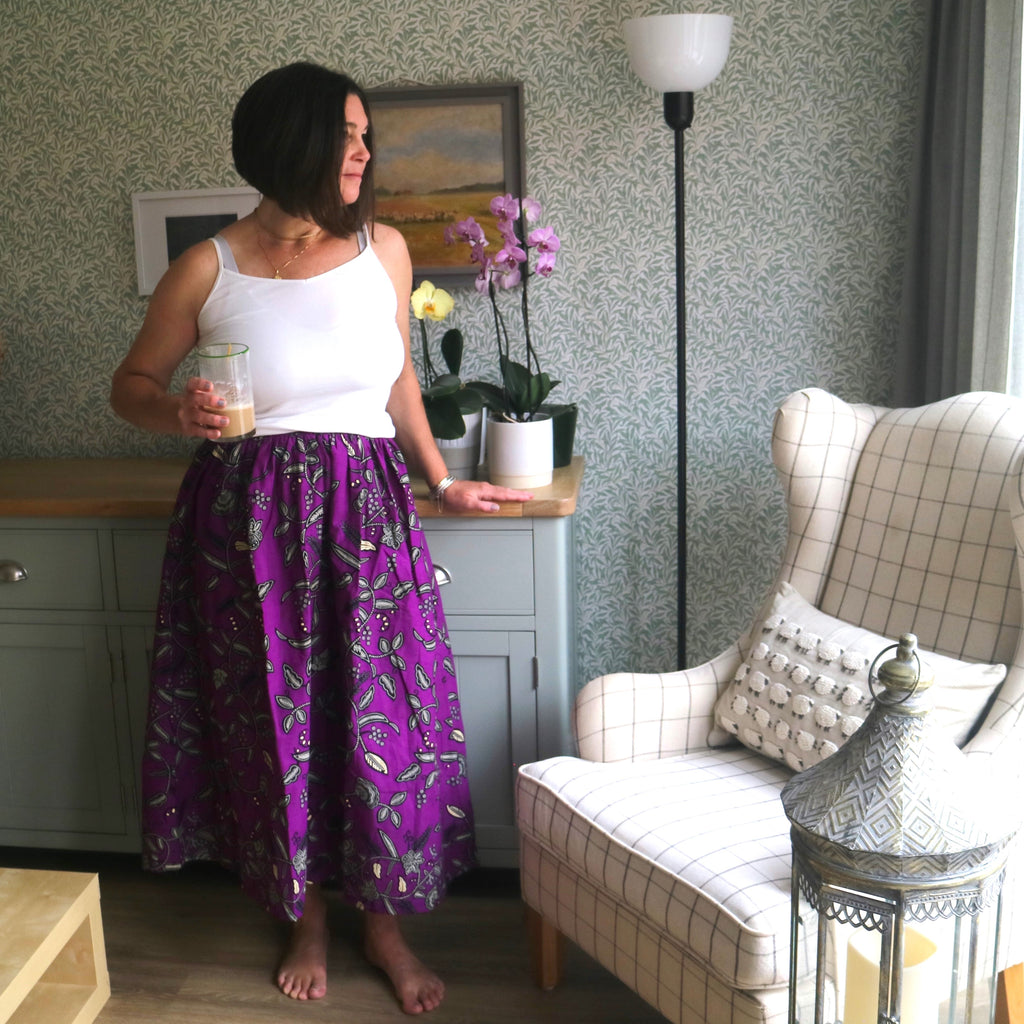 Woman in a purple skirt standing in a living room with a couch and decorative items.