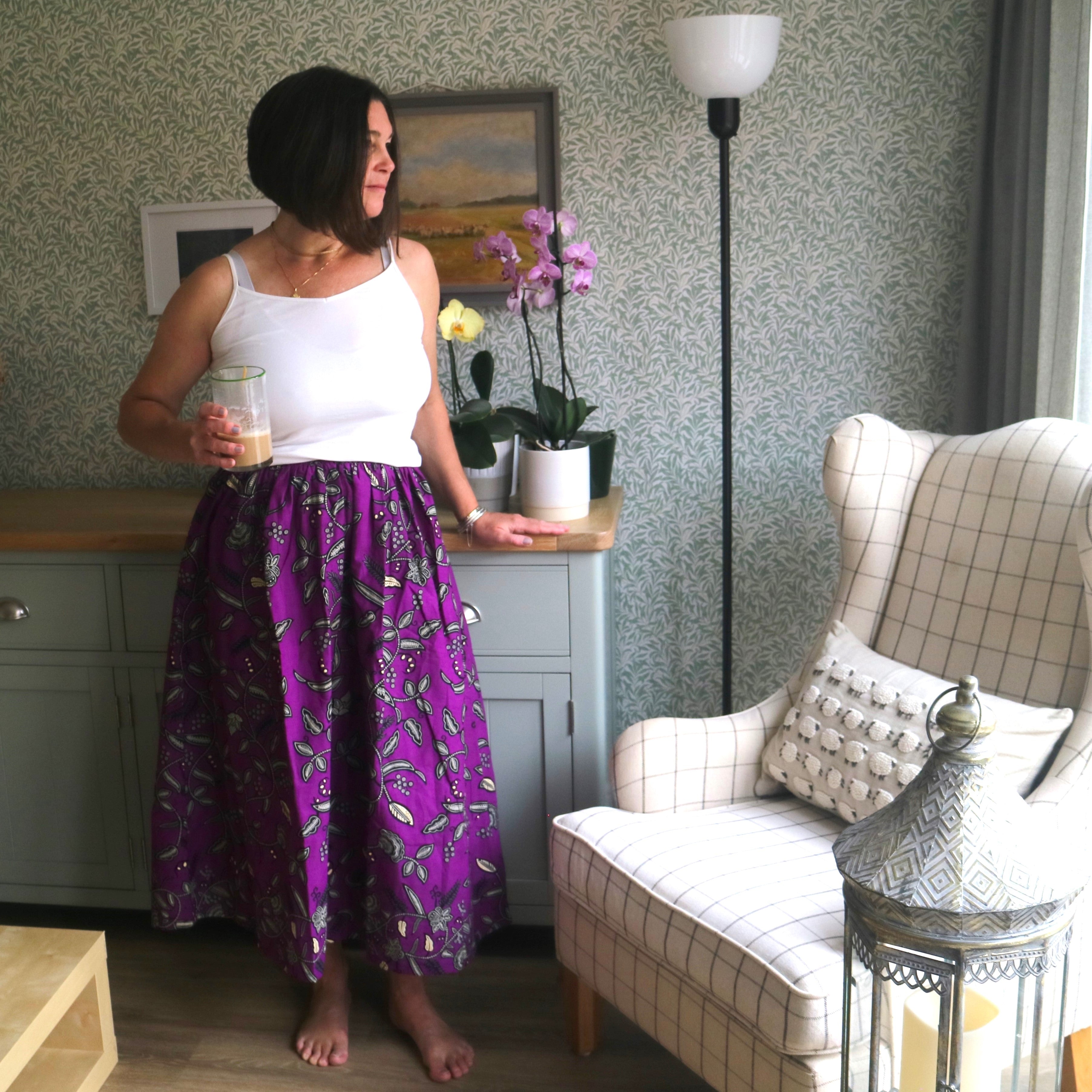 Woman in a purple skirt standing in a living room with a couch and decorative items.