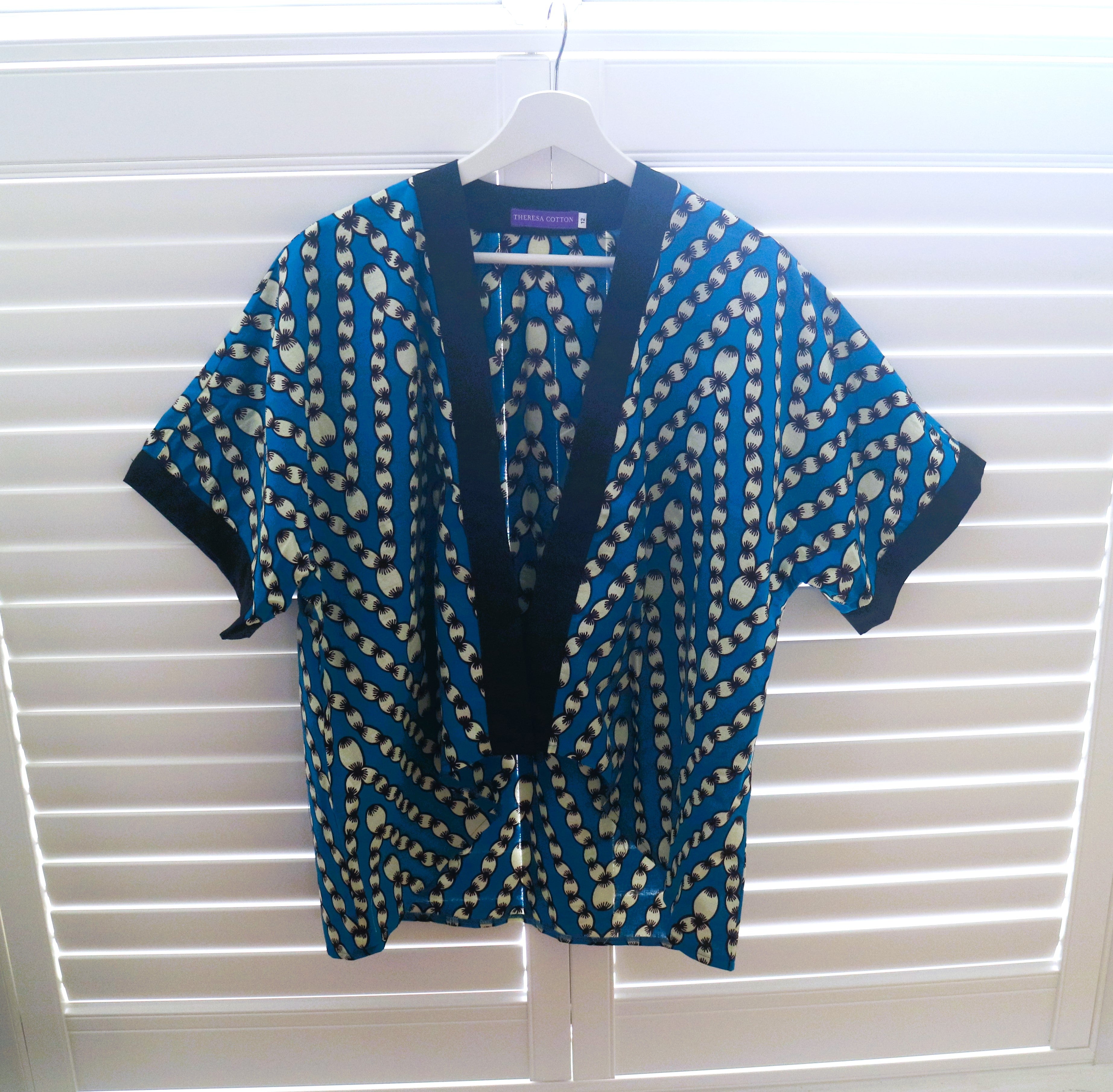 Blue and white patterned cardigan on a hanger against a white window blind background